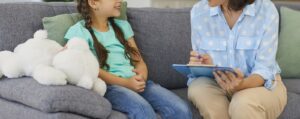 An adult smiles while taking notes and talking to a child. This could represent the support that a play therapist for children in boulder, co an offer with addressing bad behavior. Learn more about the support boulder therapists can offer for parents and their children. 
