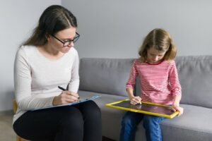 A child draws on a chalkboard while a woman writes notes. Learn how child counseling in Boulder, CO can help kids during divorce. Search for parenting support in Boulder, CO and how coparenting in Boulder, CO can offer support today. 