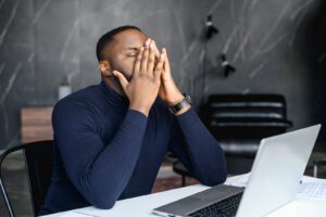 A man covers his face while sitting in front of a laptop. This could represent work stress of work that an anxiety therapist in boulder, CO can help you overcome. Learn more about anxiety treatment in Boulder, CO and how online therapy in Colorado can offer remote support. 