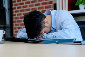 A man lays with his head on his work desk. Learn how an anxiety therapist in Boulder, CO can offer support with anxiety treatment in Boulder, CO and other services to help manage work stress. Search for online therapy in Boulder, CO today. 