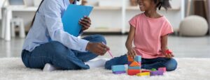 An adult points at a toy with a pencil as a child smiles at them. This could represent the benefits of working with a play therapist for children in Boulder, CO. Search for play therapy in Boulder, CO to learn more about the help online therapy in Boulder, CO can offer today. 