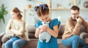 A child hugs their stuffed animal while standing between their fighting parents. This could represent the effects of divorce on kids. Learn more about blended families in Boulder, CO and how coparenting can offer parenting support in Boulder, CO 