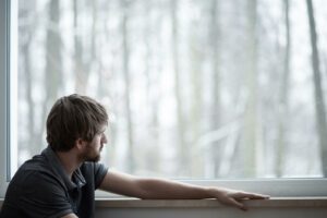 A man sits while looking out a window with a solemn expression. This could represent the effects of depression on being social. This could represent a struggle of depression that depression treatment in Boulder, CO can help address. Learn more about how a depression therapist in Boulder, CO can help you overcome depression symptoms today. 