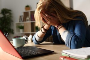 A student covers their face while sitting in front of a laptop. This could represent the academic stress that a depression therapist in Boulder, CO can help address. Learn more about other signs of depression in Boulder, CO by searching for depression in Boulder, CO today.