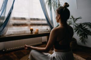 A woman practices yoga while sitting near a candle and window. Learn more about the benefits of yoga on mental health by contacting a therapist in Boulder, CO. Search for mindfulness in Boulder, CO and how mindfulness based cognitive therapy in Boulder, CO can help.